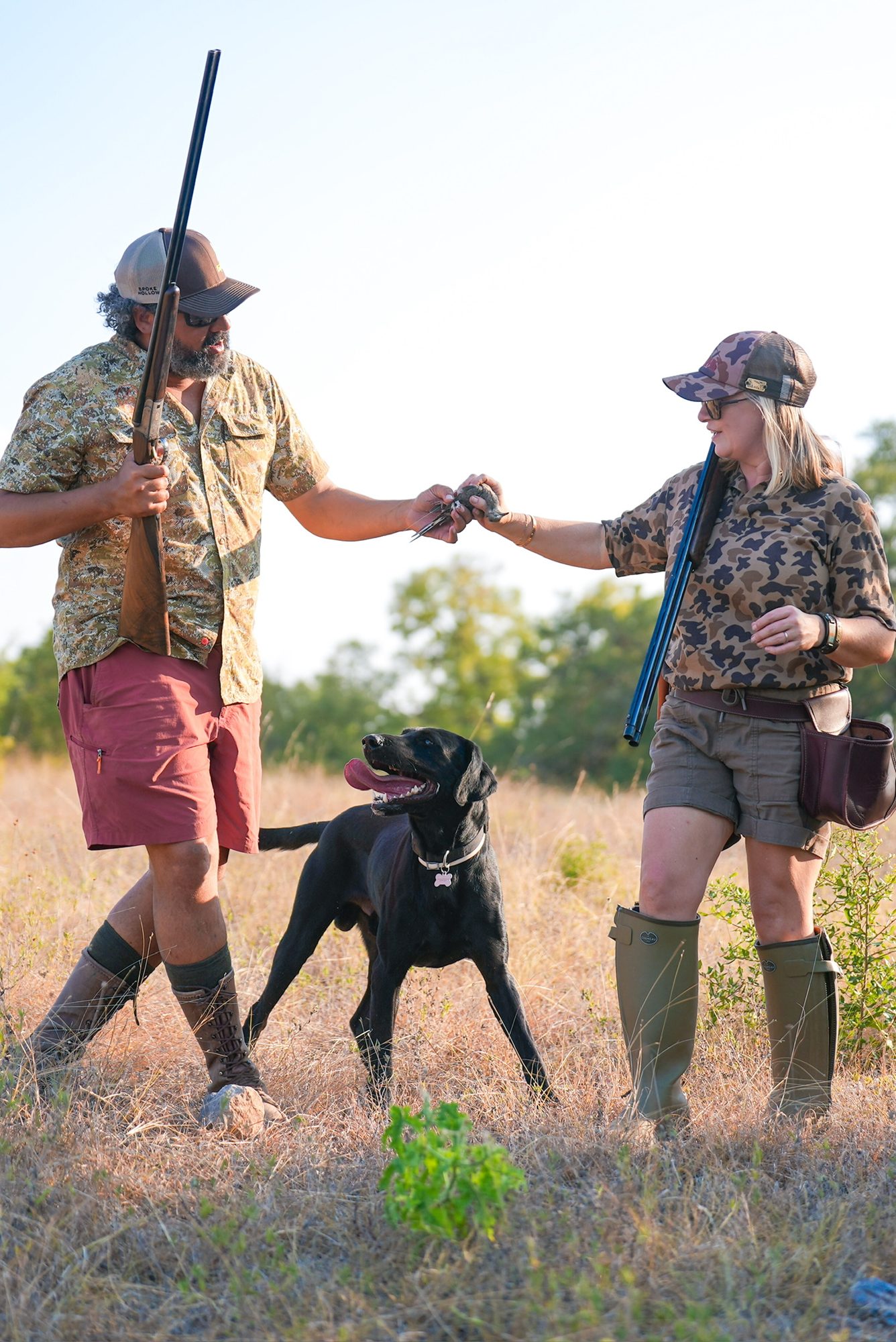 Two hunters handing off a dove as their Labrador looks on