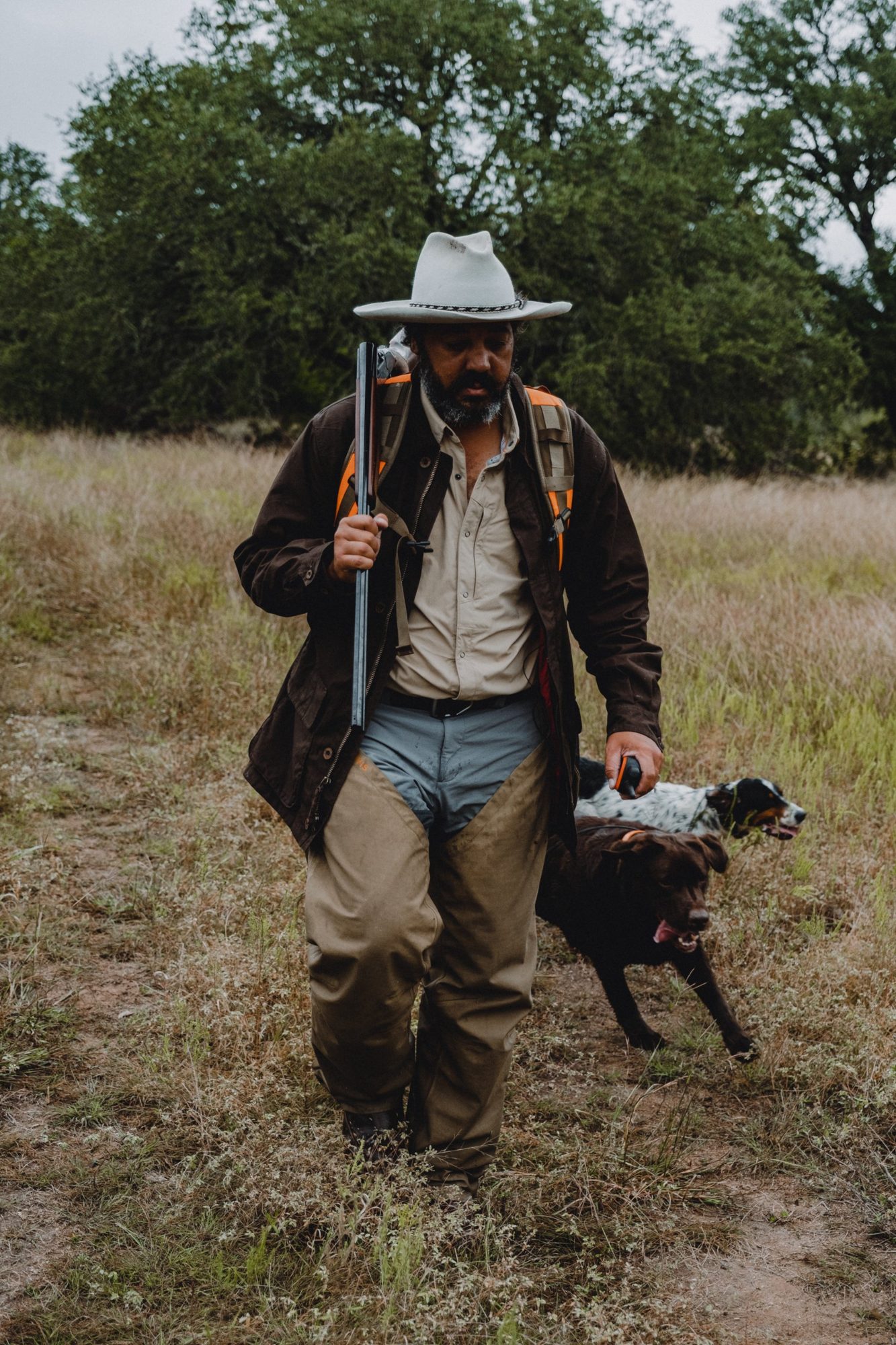 Josh walking out of the grass with a shotgun and two dogs
